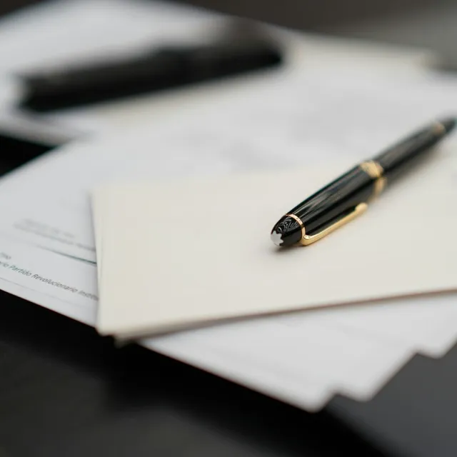 A black and gold pen resting on an envelope and papers